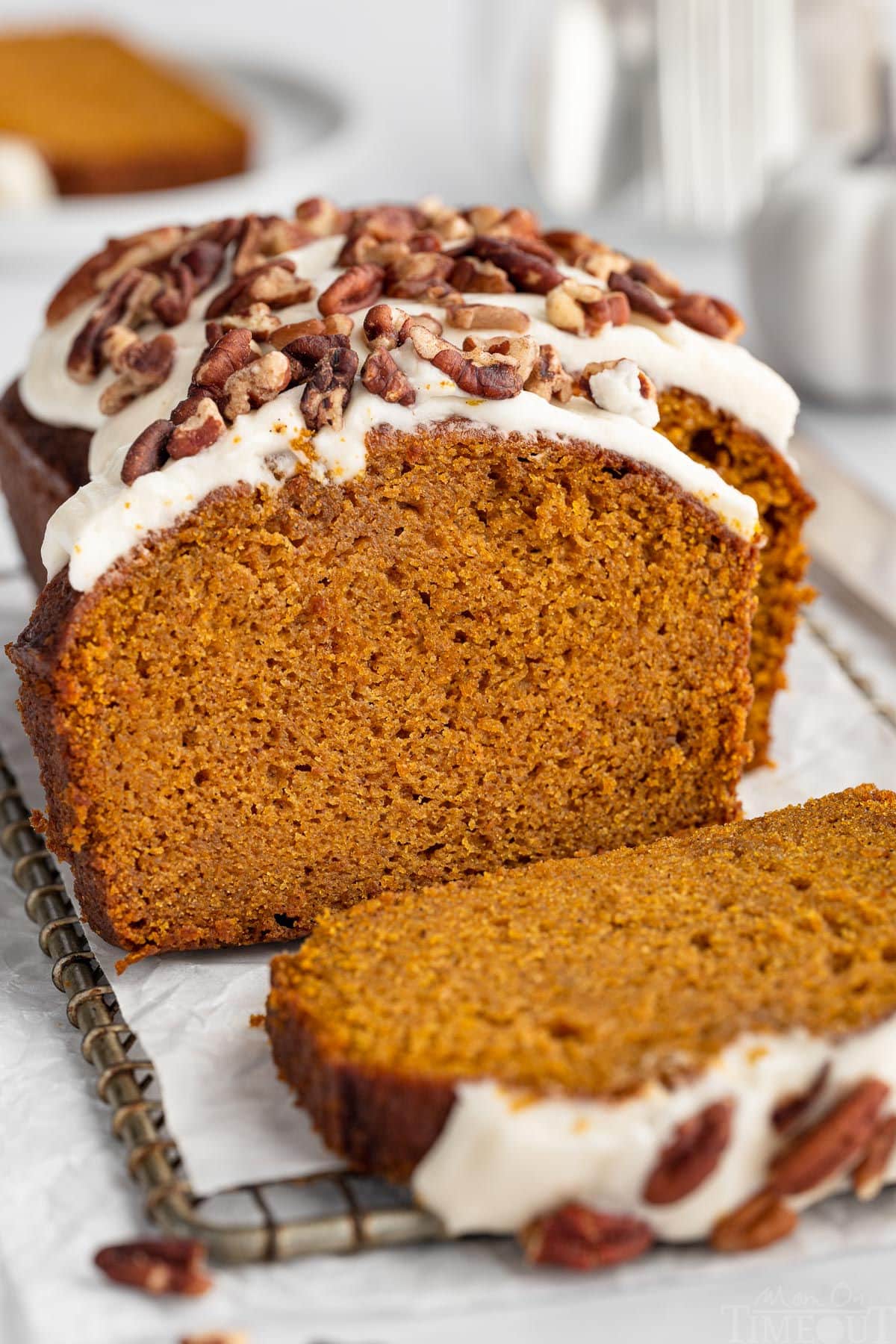 Easy pumpkin bread loaf sitting on cutting board with a few pieces sliced off. Loaf is topped with cream cheese frosting and pecans.