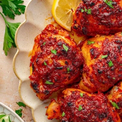 Close up shot of harissa chicken on scalloped plate with lemon wedges.