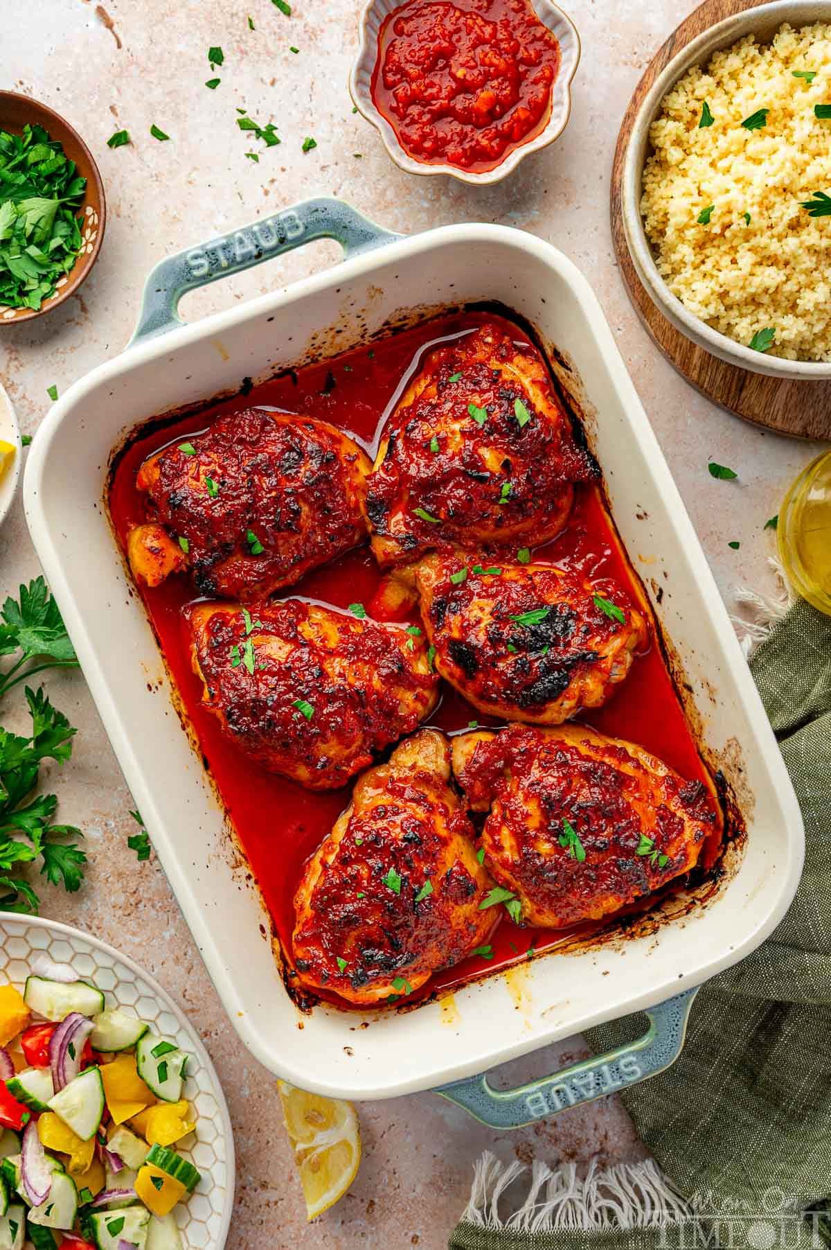 Top down shot of harissa chicken thighs in baking dish with couscous in a bowl off to the side.