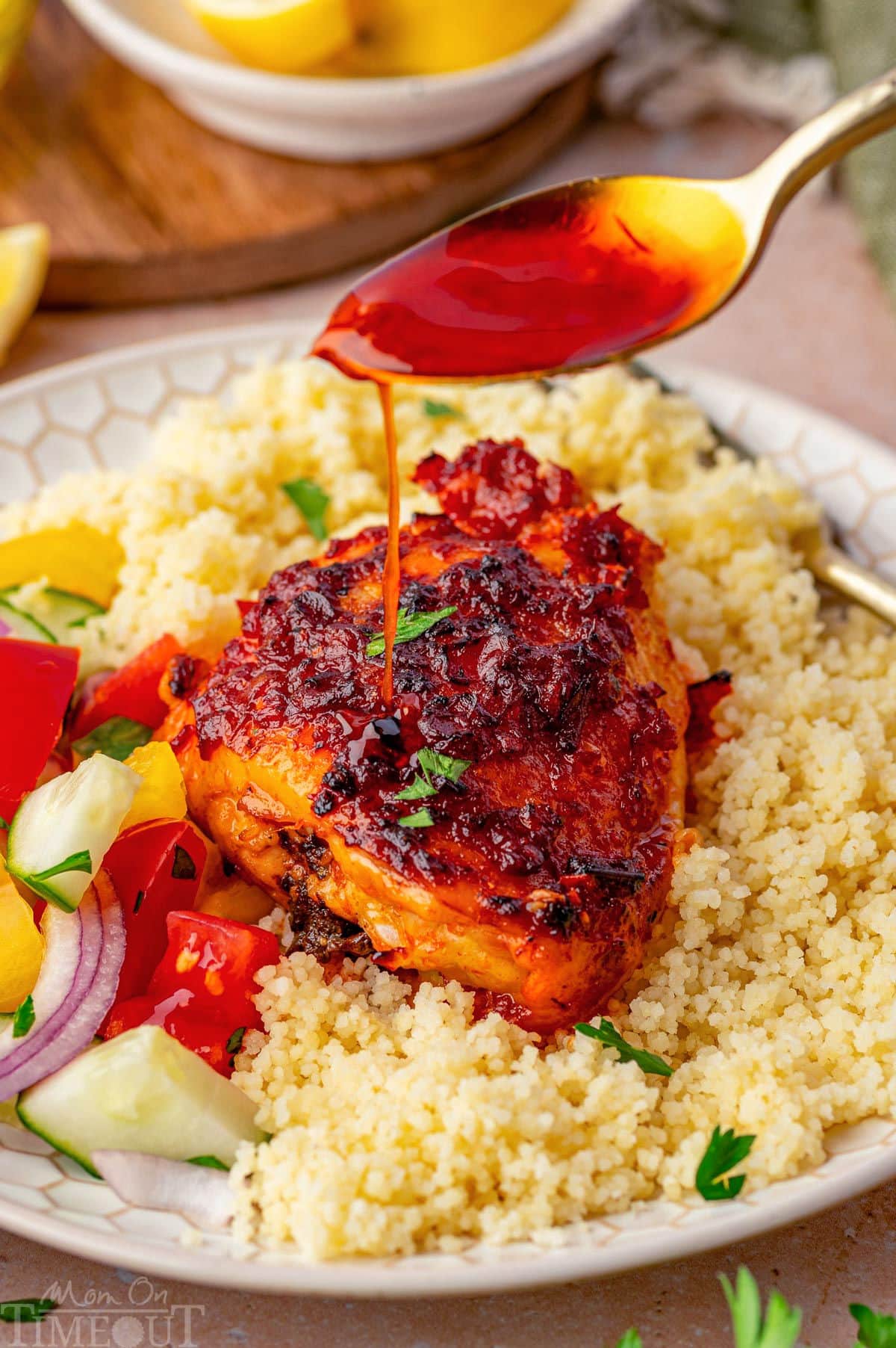 Pan sauce being drizzle on honey harissa chicken plated with couscous and fresh veggies.