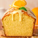 Orange pound cake with end cut off sitting on wood board topped with a glaze.