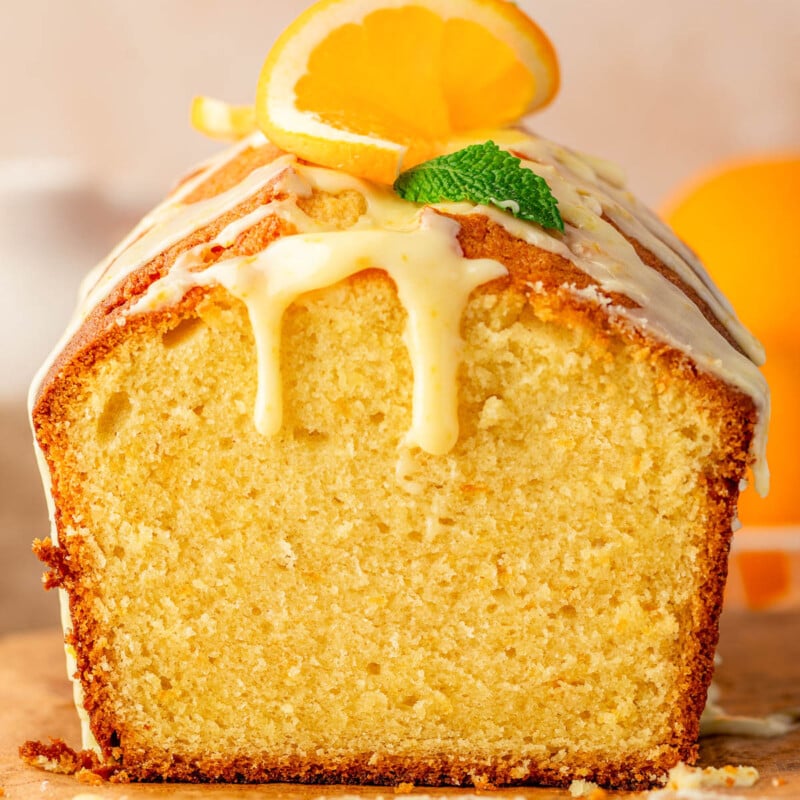 Orange pound cake with end cut off sitting on wood board topped with a glaze.