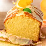 Front view of orange pound cake on wood cutting board with two slices cut off.