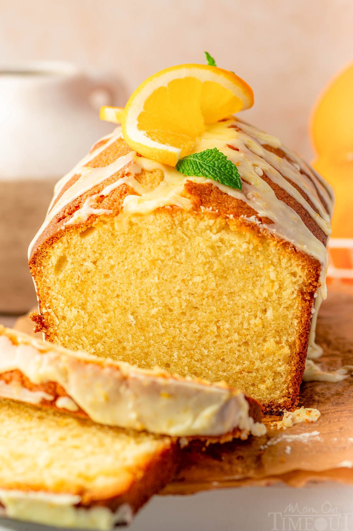 Front view of orange pound cake on wood cutting board with two slices cut off.