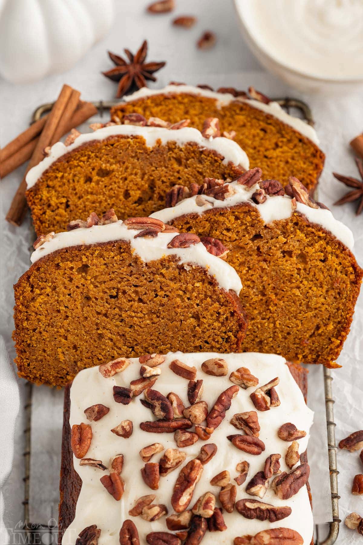 Overhead shot of pumpkin bread with cream cheese frosting on board with four slices cut and arranged on top of each other at an angle.