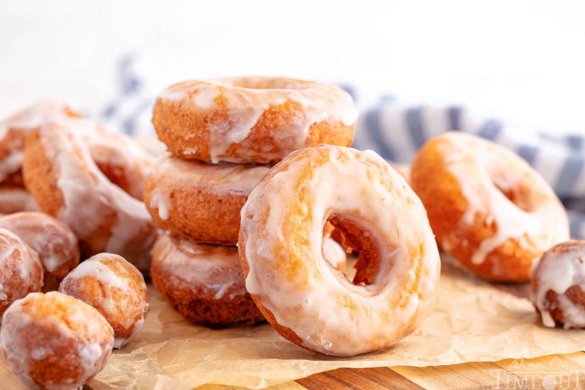 Wide shot of full batch of sour cream cake donuts on brown parchment glazed and ready to eat.