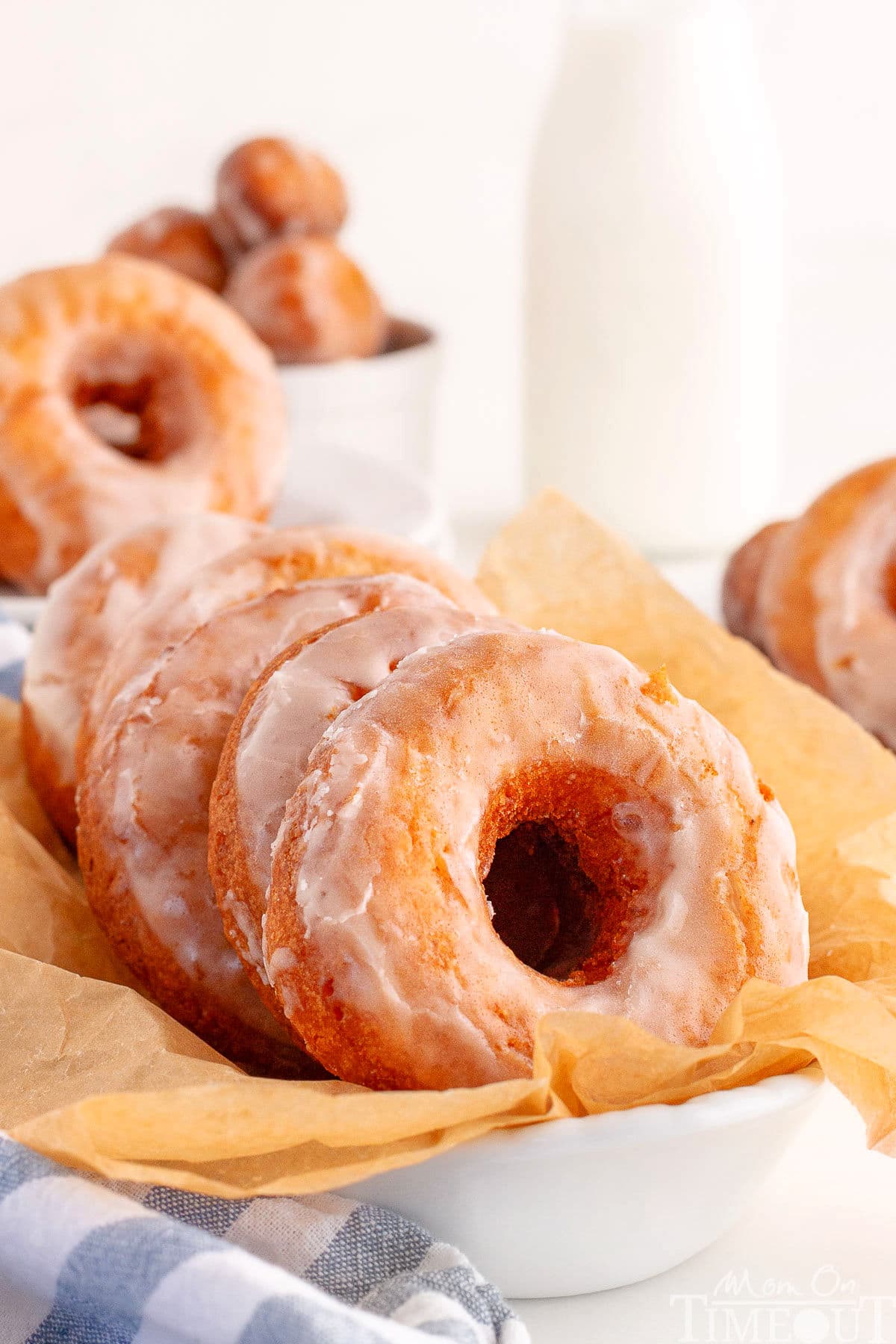 Sour Cream Cake Donuts in white dish lined with parchment. More donuts can be seen in the background.