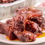 Shot of st louis ribs on white round plate with the rest of the party ribs in a foil pan in the background.