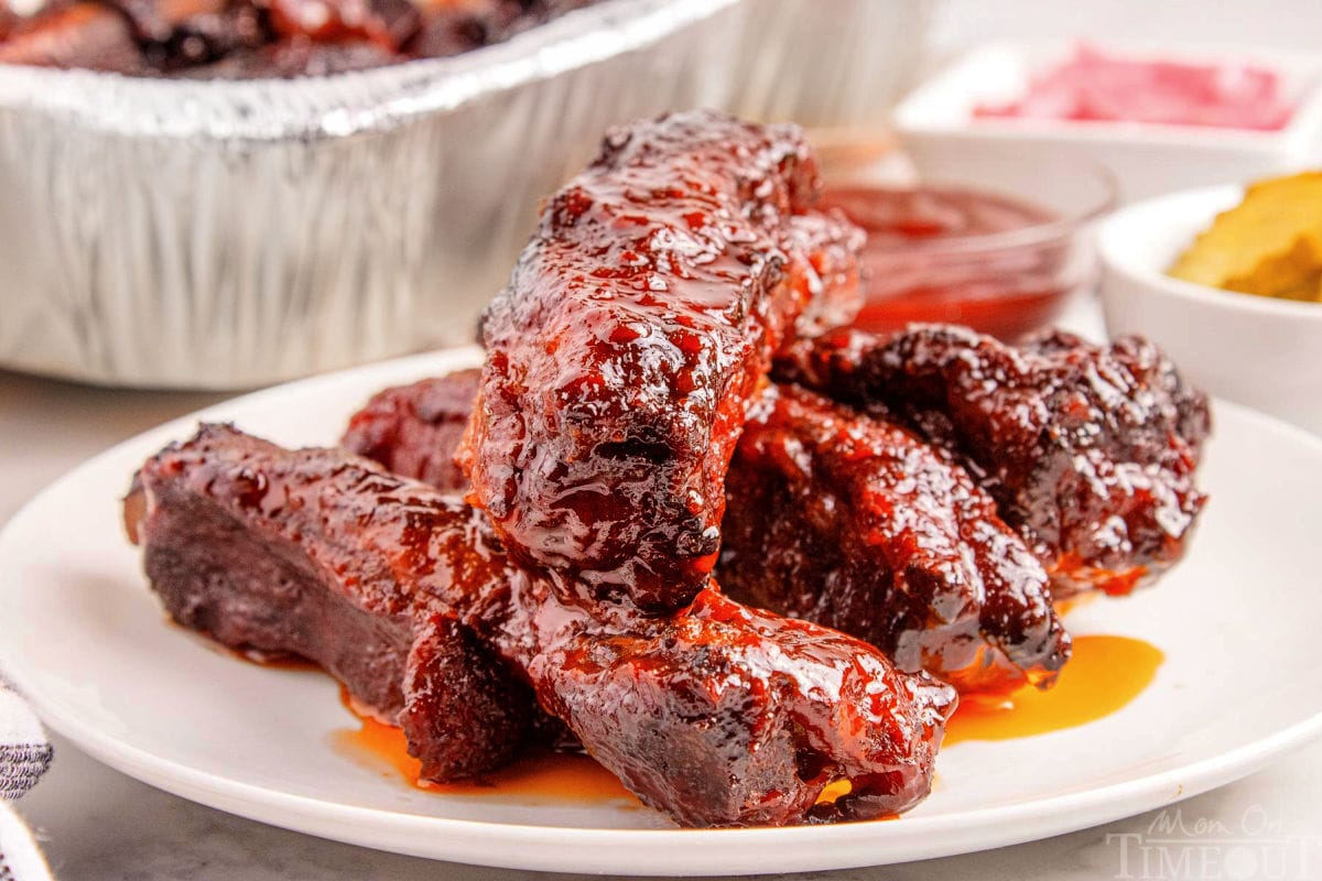 Shot of st louis ribs on white round plate with the rest of the party ribs in a foil pan in the background.