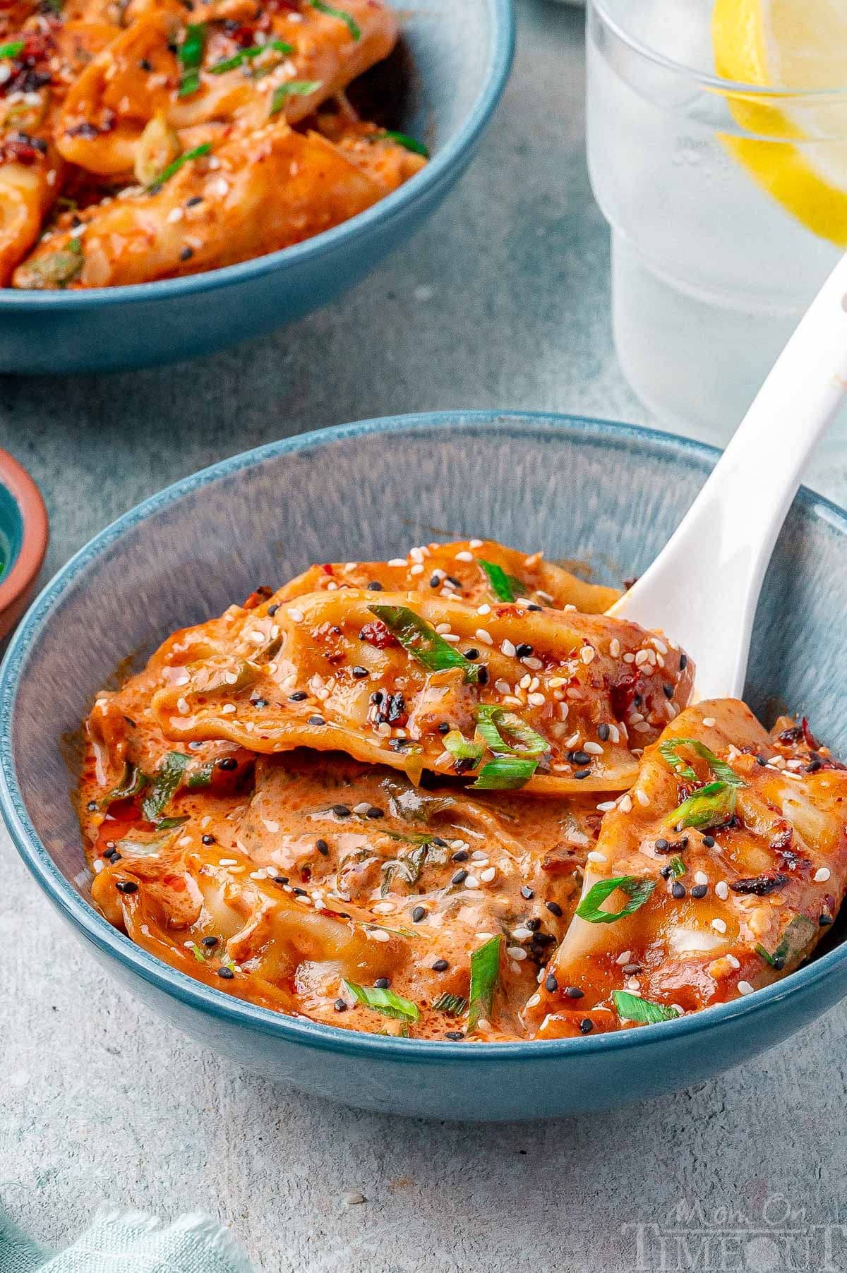 Bowl of baked dumplings garnished with green onions, sesame seeds and chili crisp.