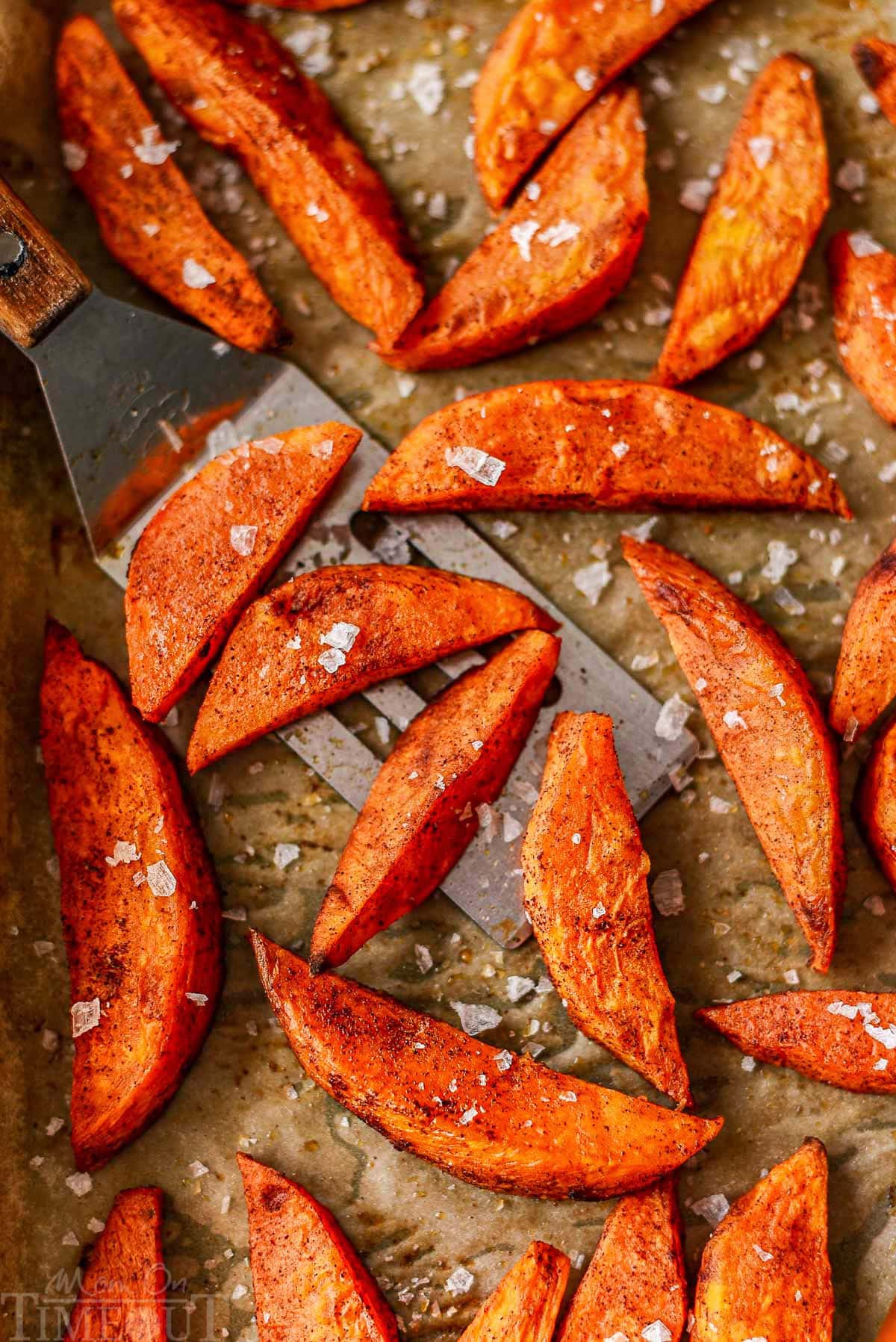 Top down look at roasted sweet potato wedges on parchment lined baking sheet.