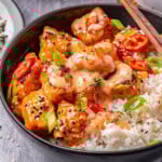 Close up shot of bang bang salmon bites in black bowl served with rice and topped with green onions and sesame seeds.