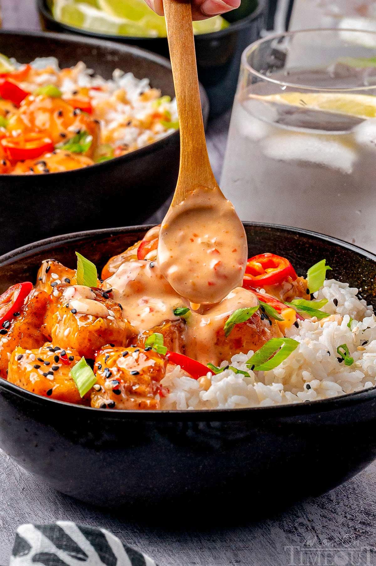 Shot of bang bang sauce being drizzled on bowl of salmon bites.