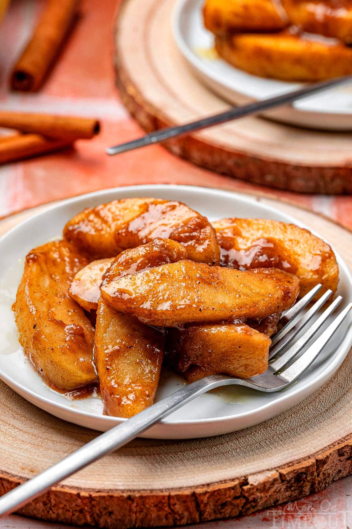 Serving of fried apples on a small white round plate with a fork resting on the edge.