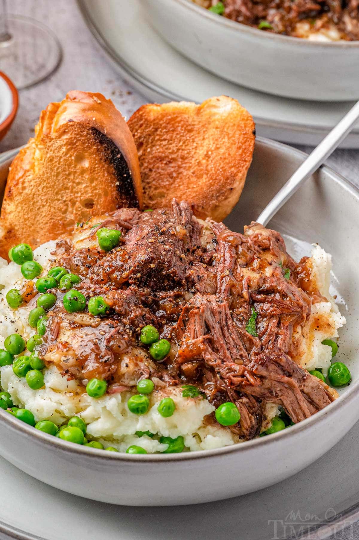 Close up shot of french onion soup pot roast in bowl with mashed potatoes, peas and french bread.