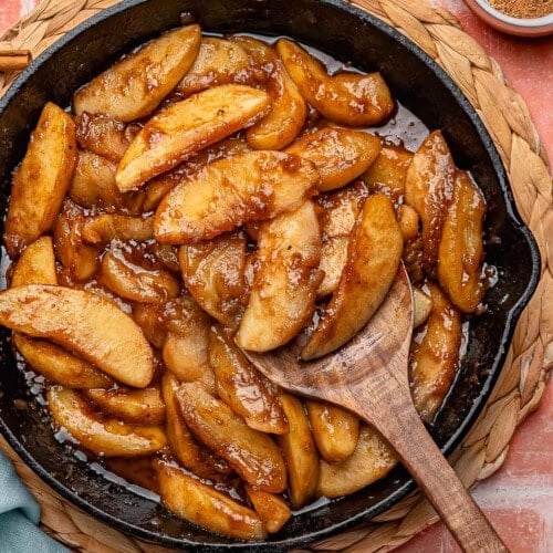 Overhead shot of fried apples in cast iron skillet. Spices and sugar in small bowls around it.