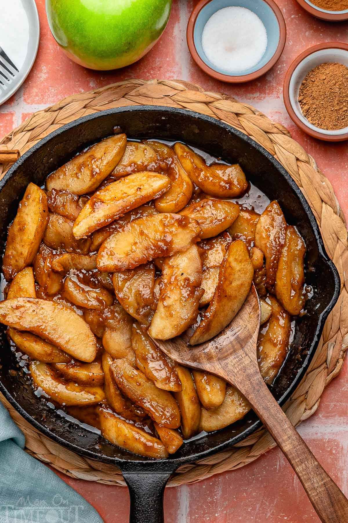 Overhead shot of fried apples in cast iron skillet. Spices and sugar in small bowls around it.