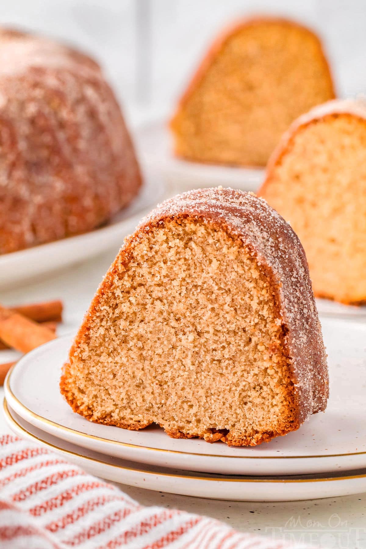 Piece of apple cider donut cake on round white plate. More pieces can be seen in the background.
