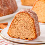 Piece of apple cider donut cake on round white plate. More pieces can be seen in the background.