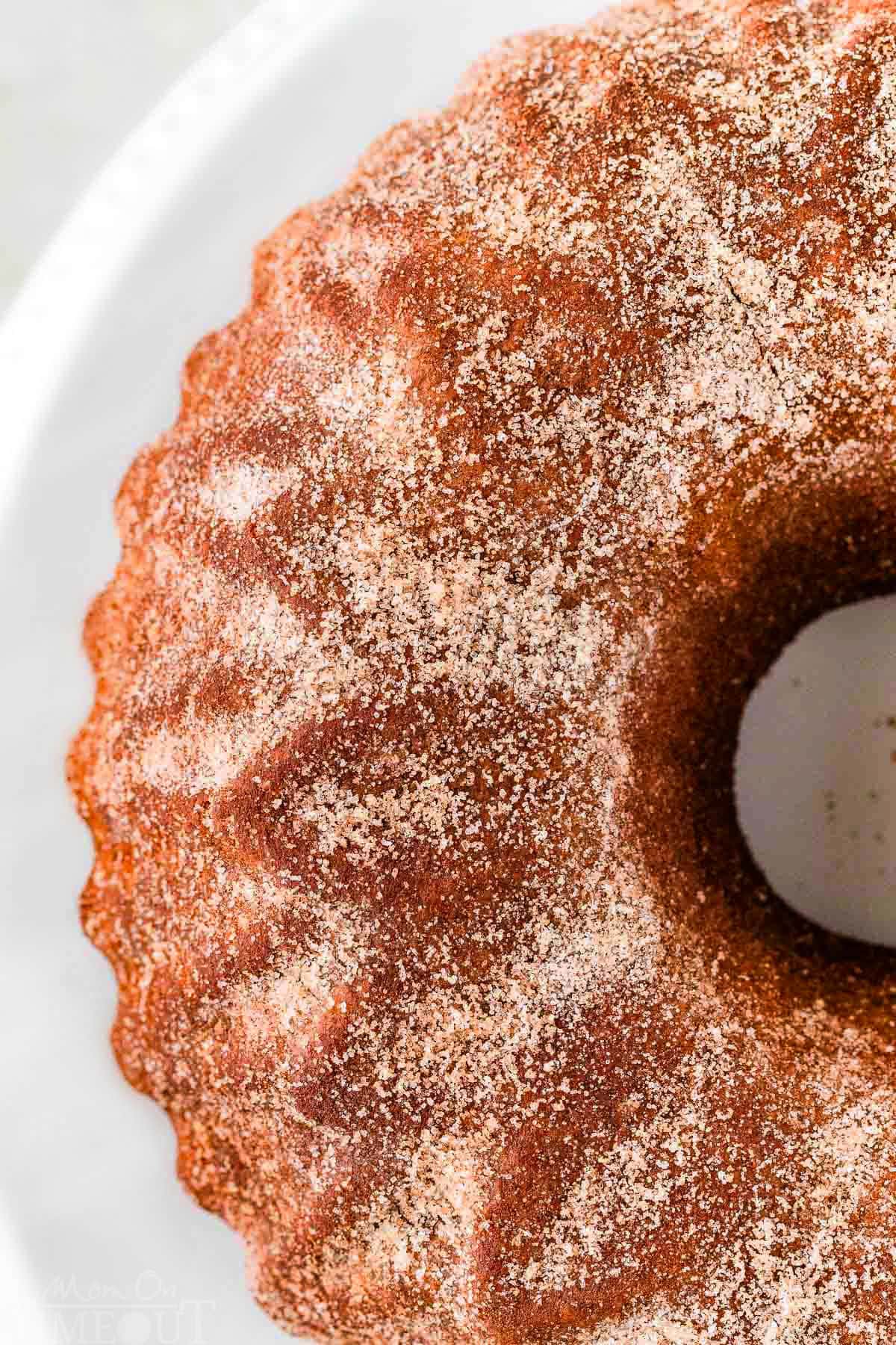 Top down view of half the apple cider donut cake whole on a white cake stand.