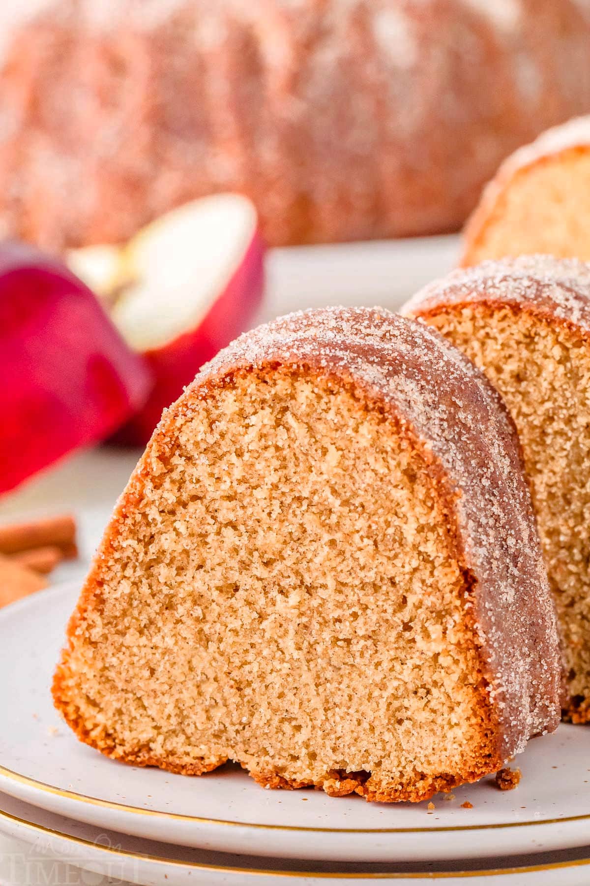 Piece of apple cider donut cake on round white plate. More pieces can be seen in the background.