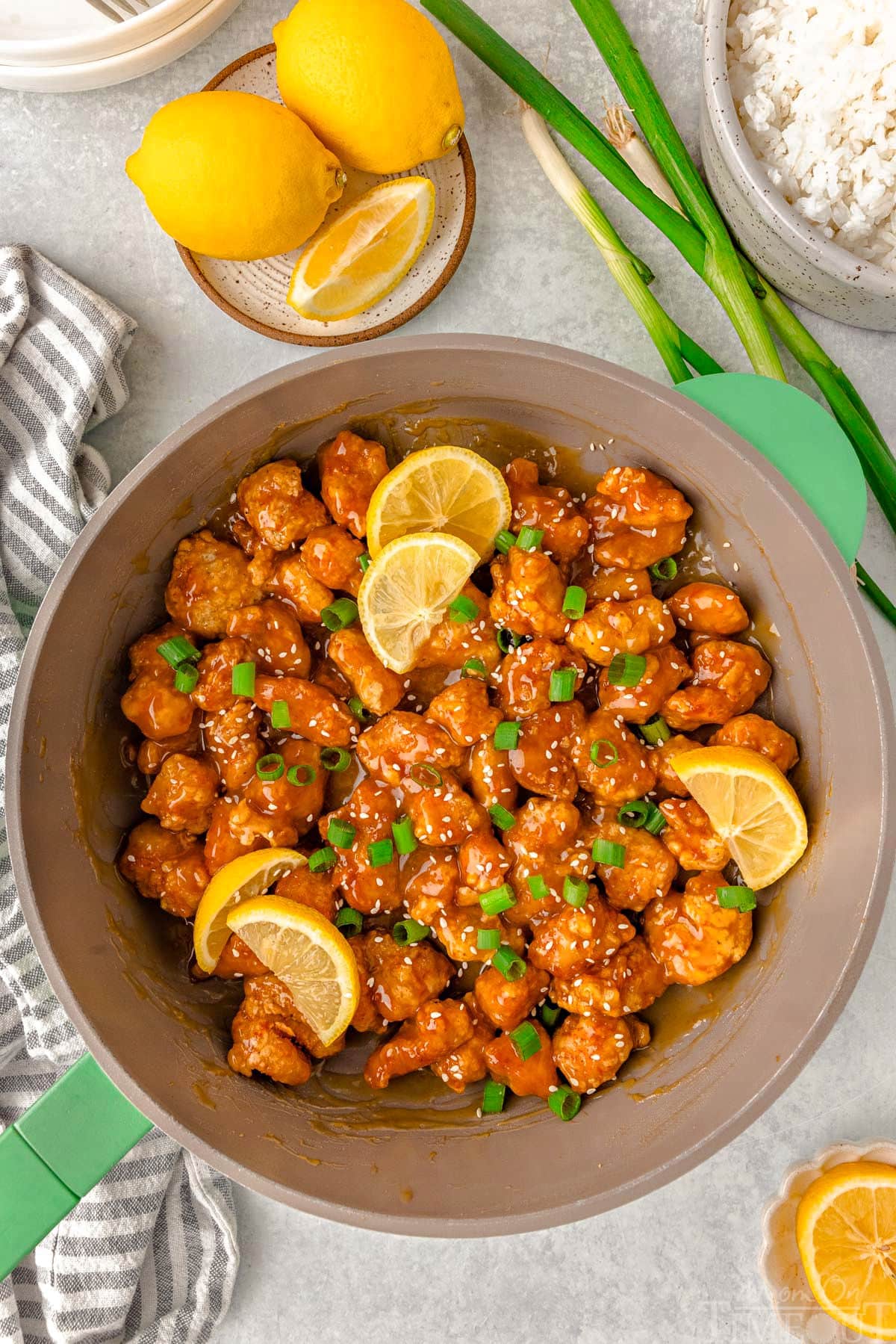 Overhead shot of skillet of chinese lemon chicken ready to be served. Garnished with slices of lemon and green onions.