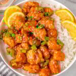 Overhead shot of lemon chicken and white rice on round plate with lime slices and green onions for garnish.