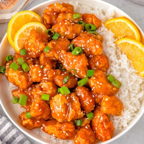 Overhead shot of lemon chicken and white rice on round plate with lime slices and green onions for garnish.