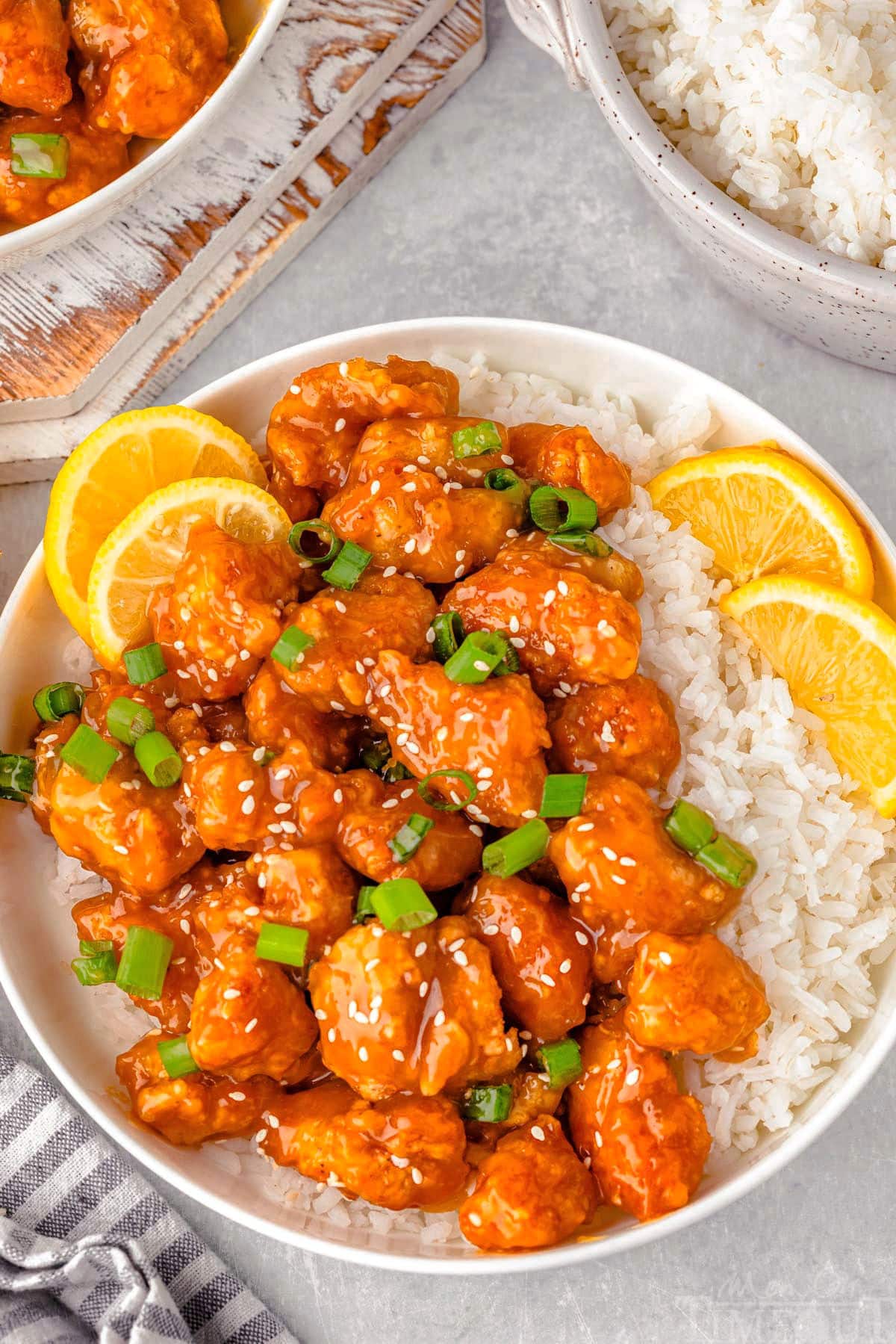 Overhead shot of lemon chicken and white rice on round plate with lime slices and green onions for garnish.
