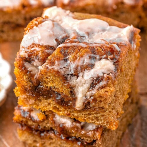 Two pieces of cinnamon roll pumpkin focaccia stacked on a wood surface with more focaccia in the background.
