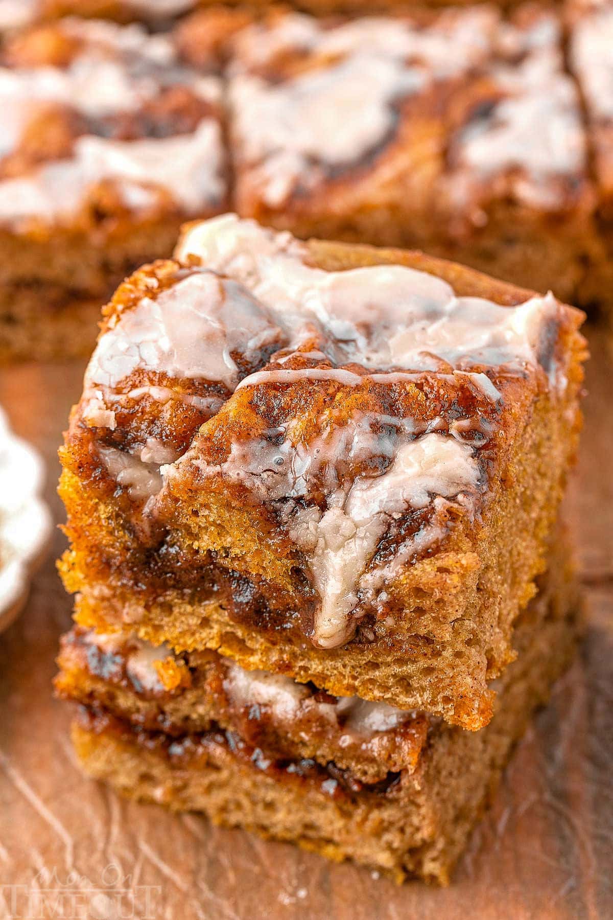 Two pieces of cinnamon roll pumpkin focaccia stacked on a wood surface with more focaccia in the background.