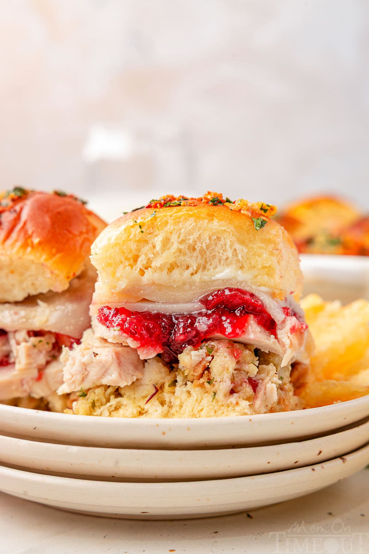 Two Turkey sliders sitting on small round plates stacked three high. Cranberry sauce, juicy turkey, and stuffing can all be seen in between the soft hawaiian roll.
