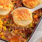 Angled overhead shot of ground beef pot pie with biscuit topping in casserole dish with one serving removed. Five biscuits remain.