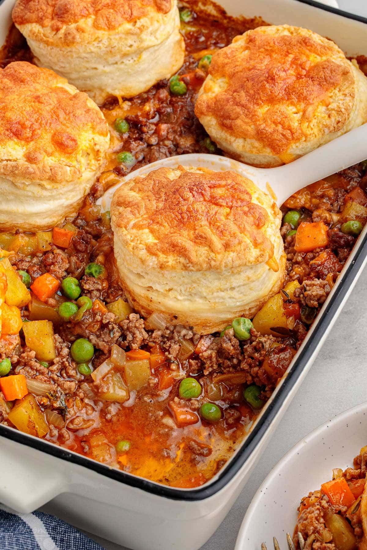 Angled overhead shot of ground beef pot pie with biscuit topping in casserole dish with one serving removed. Five biscuits remain.