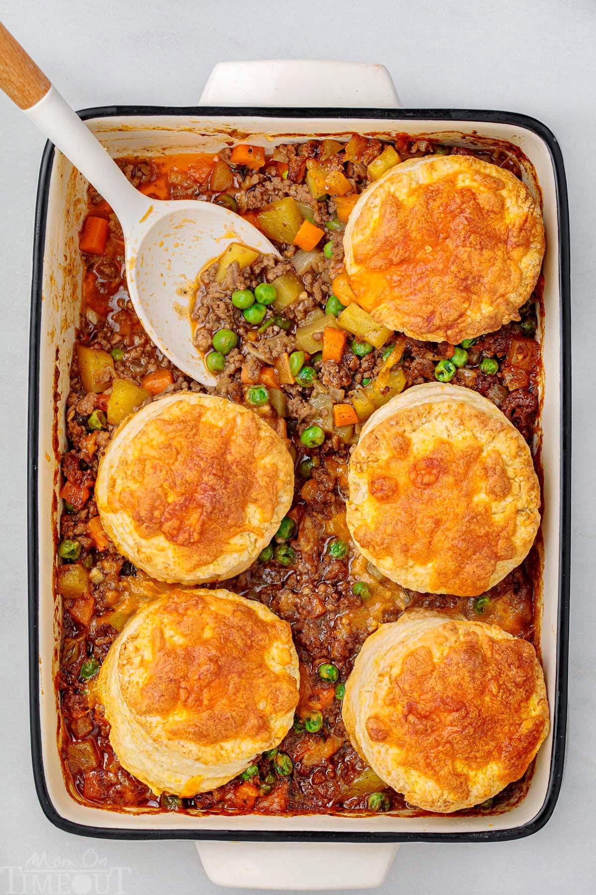 Overhead shot of ground beef pot pie topped with biscuits. One biscuit and serving has been removed from casserole dish.