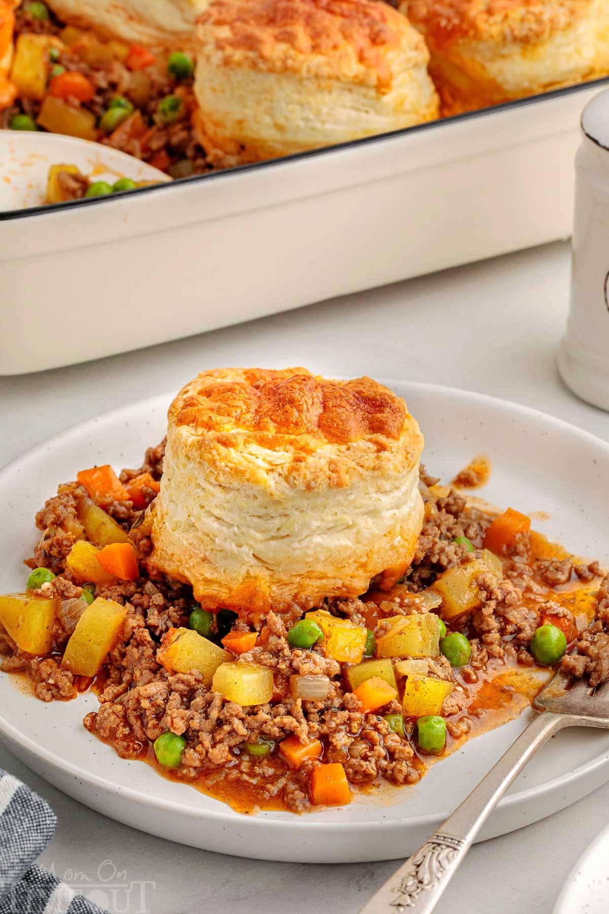 Small round white plate topped with hamburger beef pot pie which has been made with biscuits.