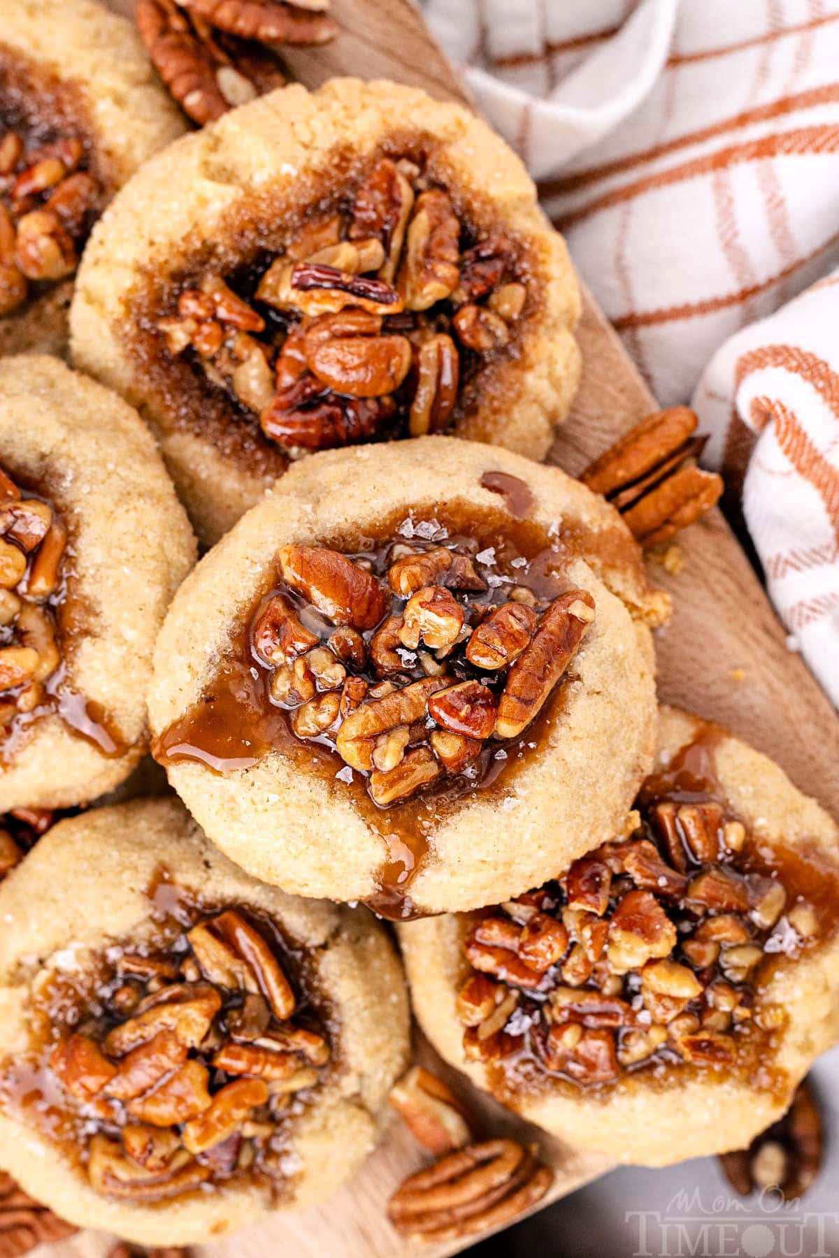 Overhead shot of pecan pie cookies piled high on a wood board next to a checked linen.