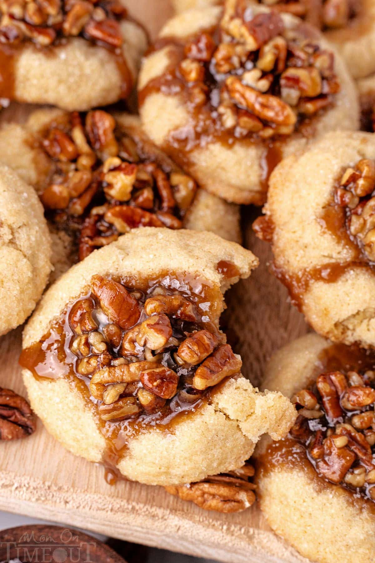 Shot of pecan pie cookies recipe piled on wood board. Top cookie has a bite taken out of it.