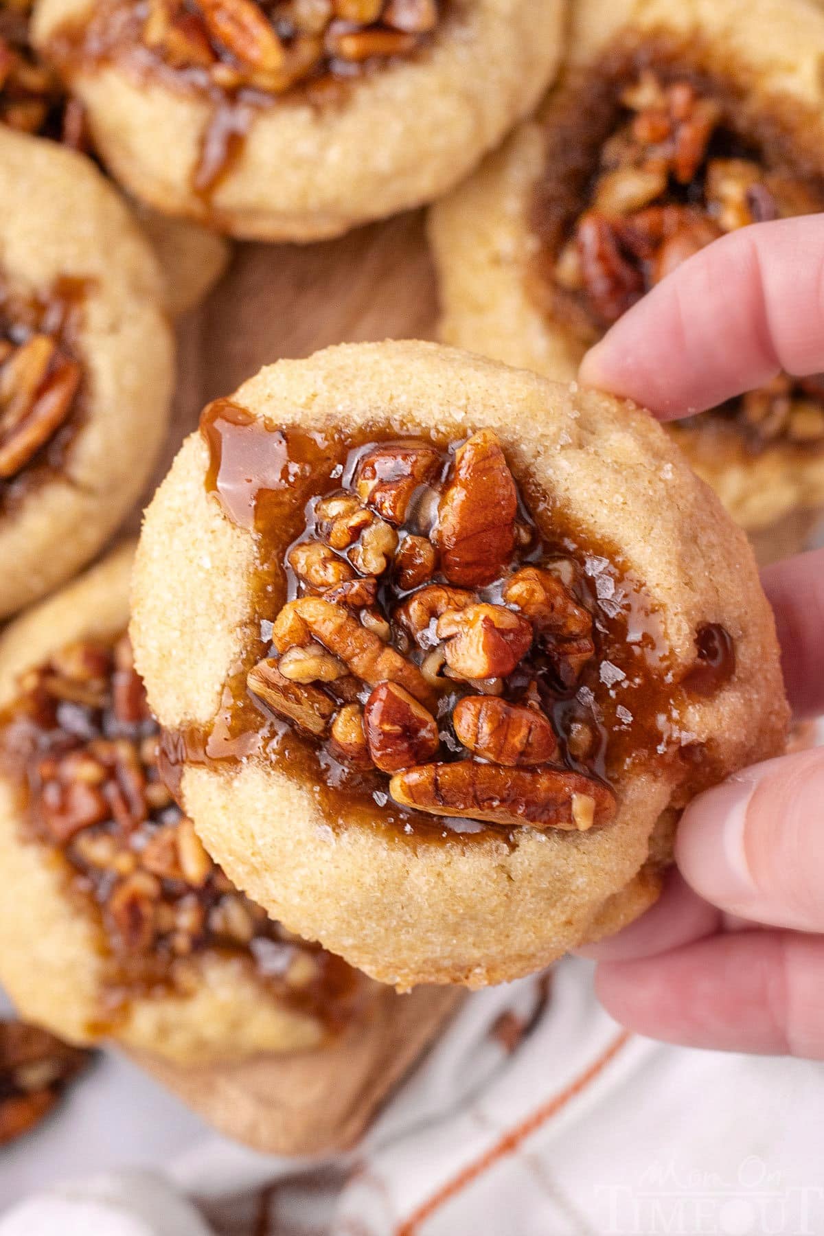 Pecan pie thumbprint cookies lifted off the board with a hand.