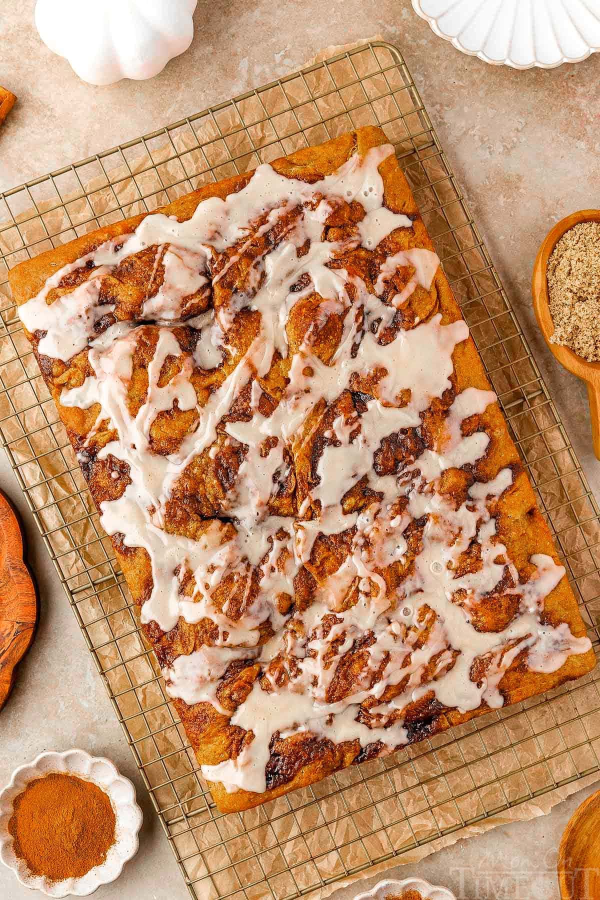 Overhead shot of pumpkin cinnamon roll focaccia recipe on cooling rack drizzled with maple glaze.