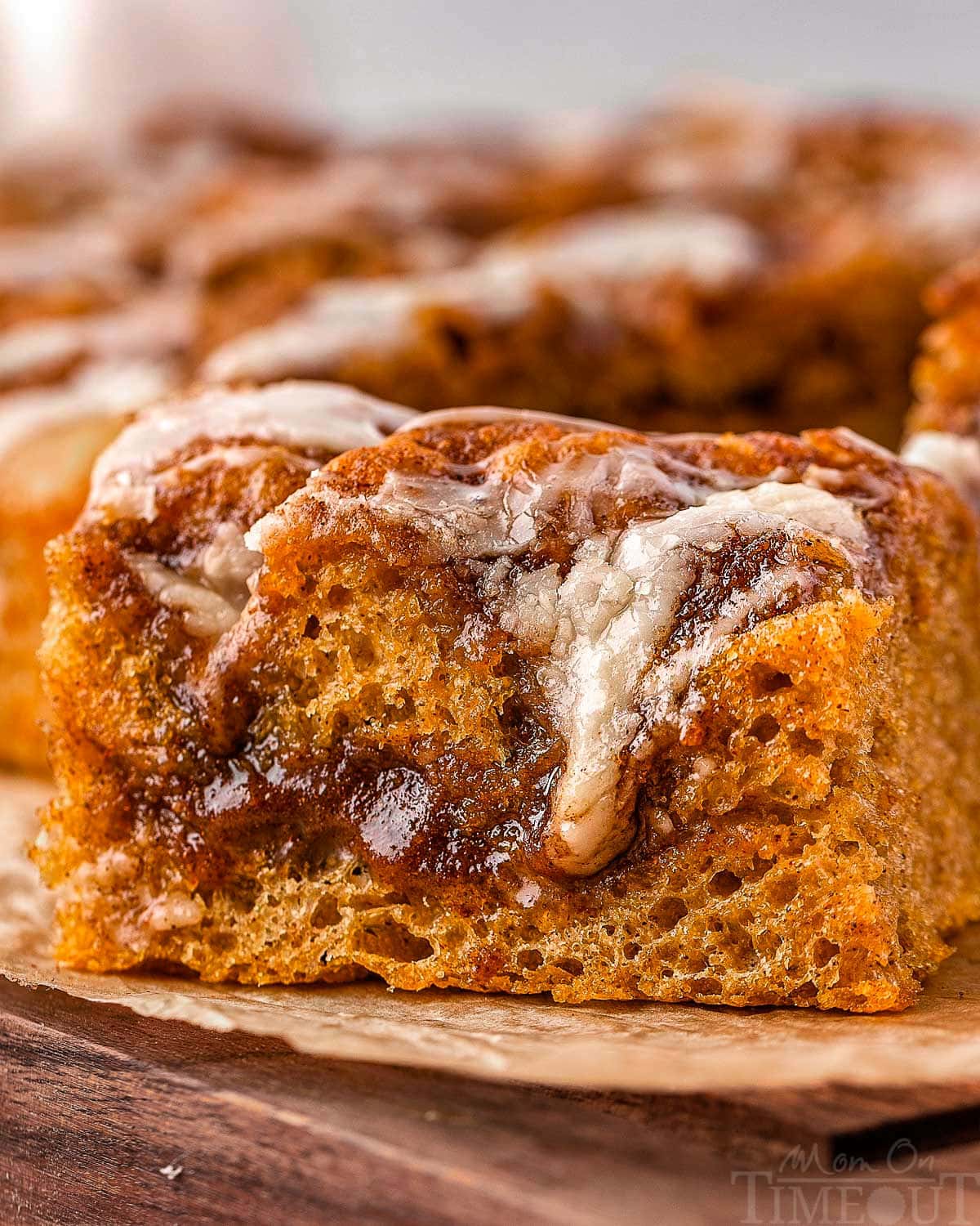 Piece of pumpkin cinnamon roll focaccia sitting on brown parchment on a wood cutting board.