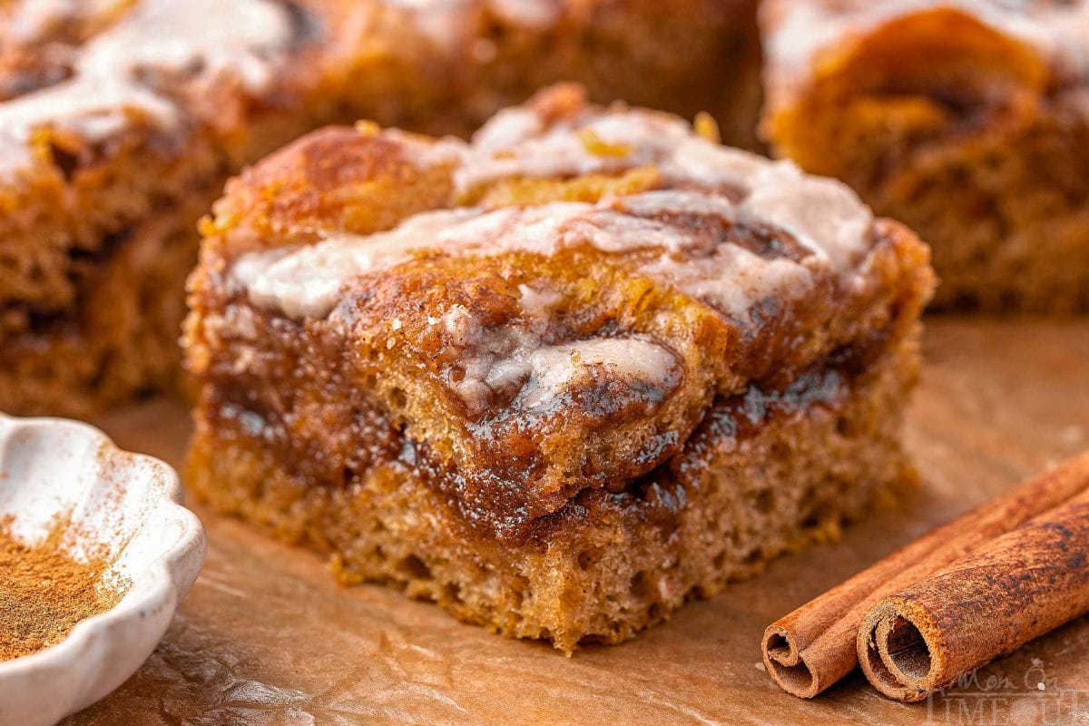 Wide shot of pumpkin focaccia cinnamon roll on brown parchment next to cinnamon stick.