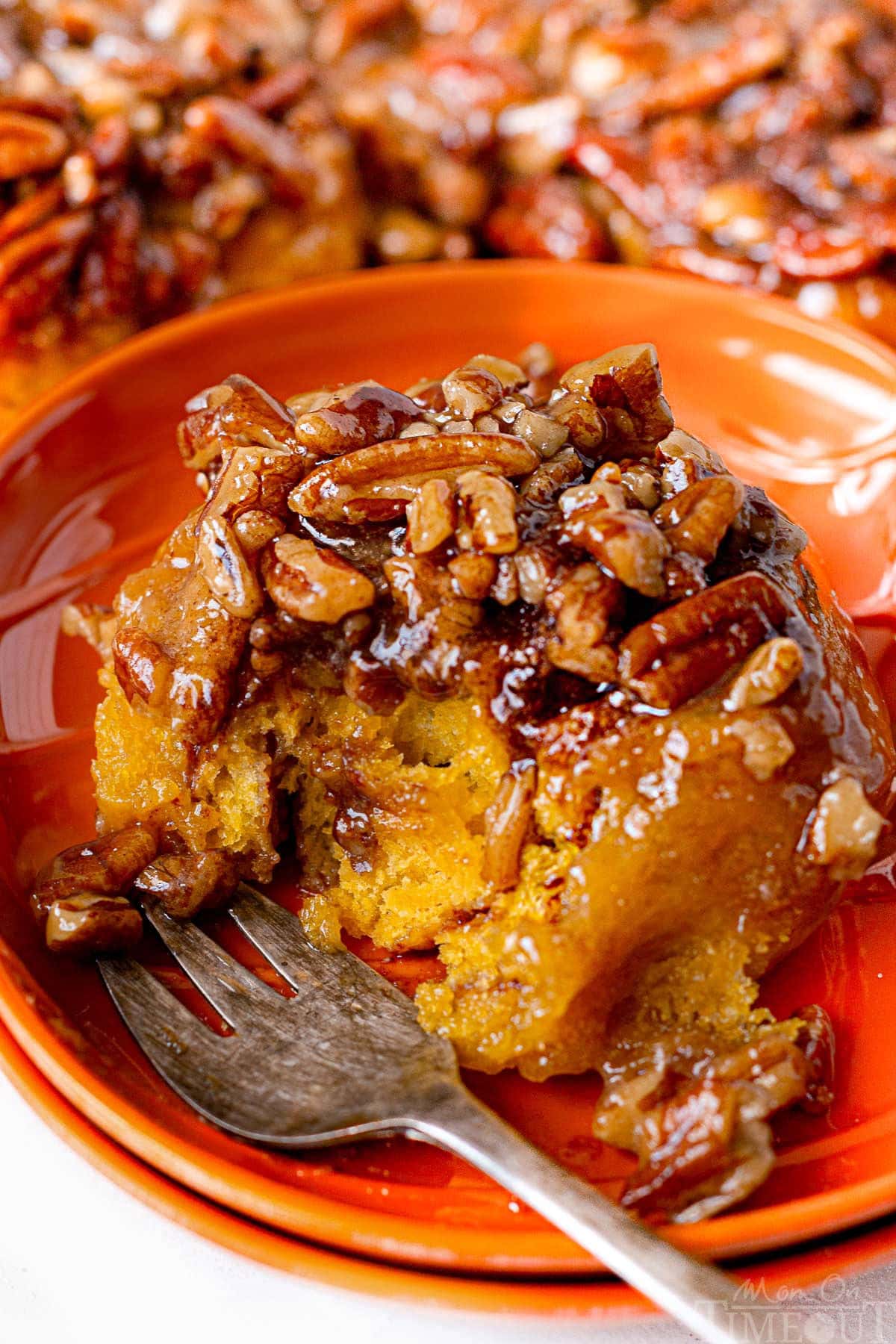 Pumpkin sticky bun on orange plate with fork. One bite has been taken out of the bun.