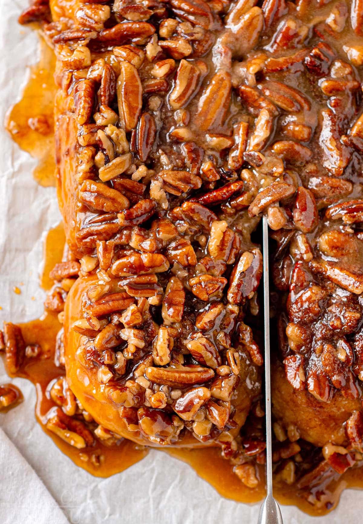 Overhead view of sticky bun being cut away from the remaining buns on a parchment lined cutting board.