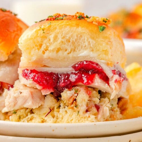 Two Turkey sliders sitting on small round plates stacked three high. Cranberry sauce, juicy turkey, and stuffing can all be seen in between the soft hawaiian roll.