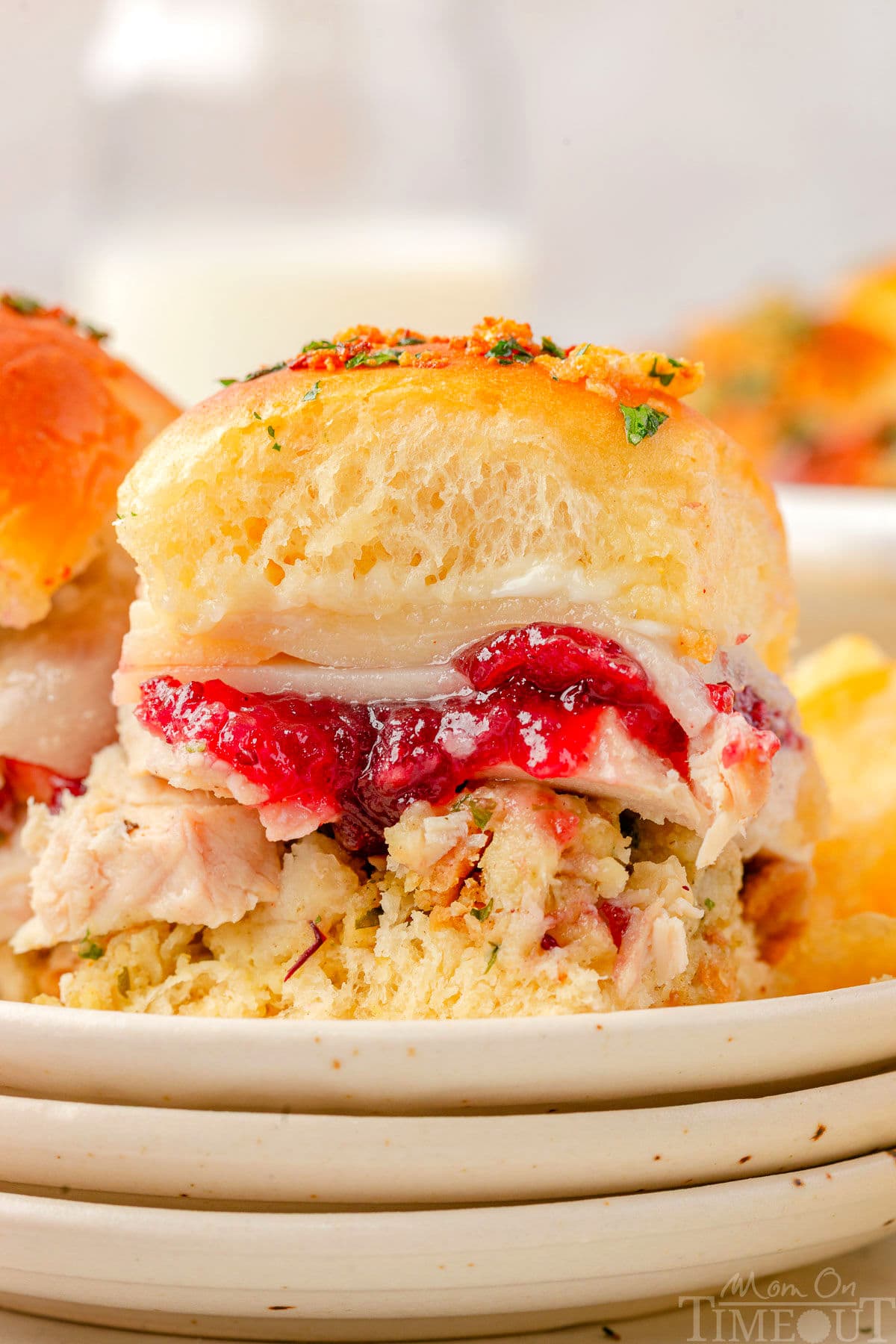 Turkey slider sitting on small round plates stacked three high. Cranberry sauce, juicy turkey, and stuffing can all be seen in between the soft hawaiian roll.
