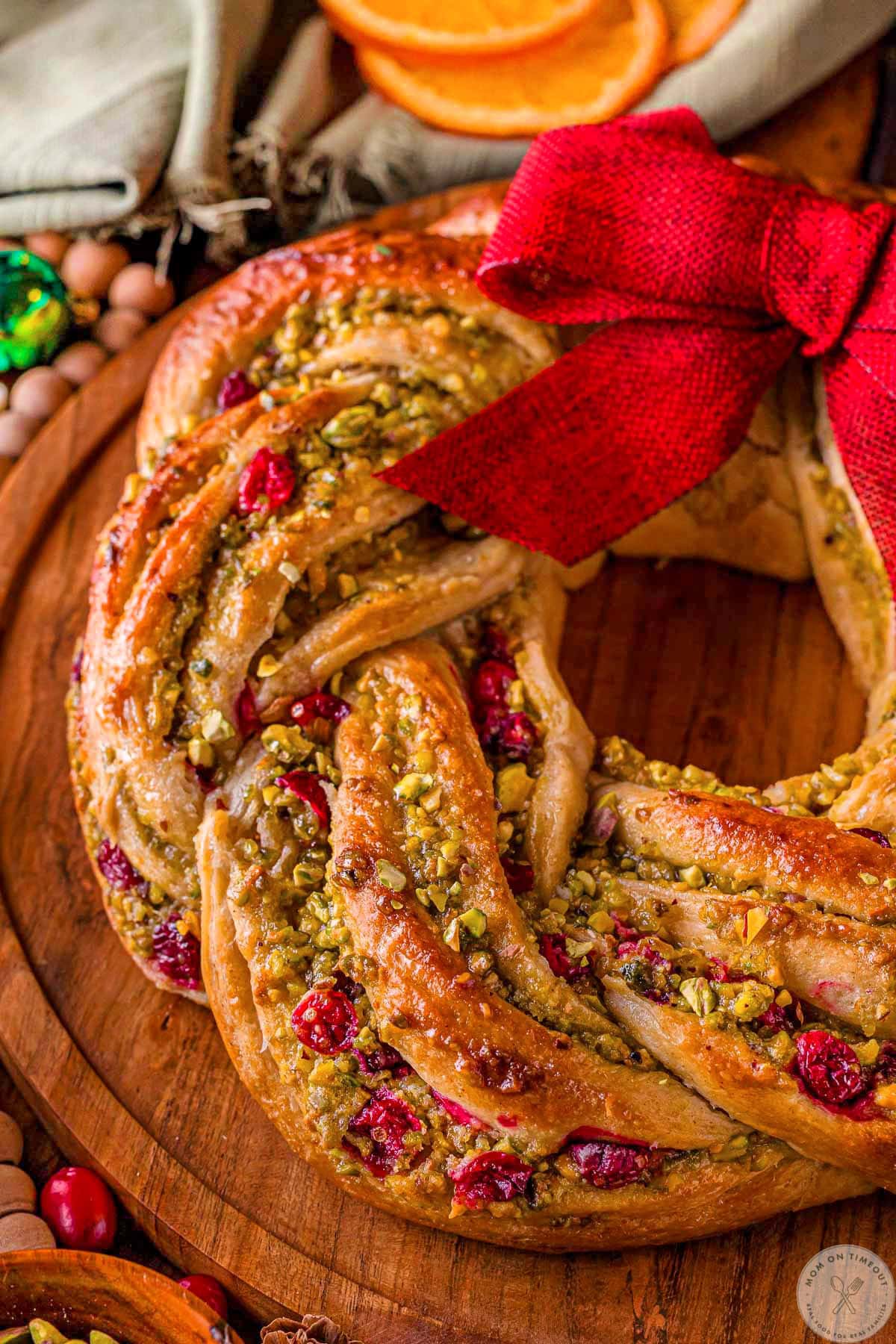 Angled overhead shot of babka wreath decorated for the holidays and made with pistachios and cranberries. A bow is tied at the top of the babka.