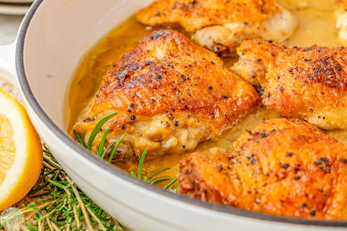 Wide shot of chicken thighs that have braised in a white skillet.