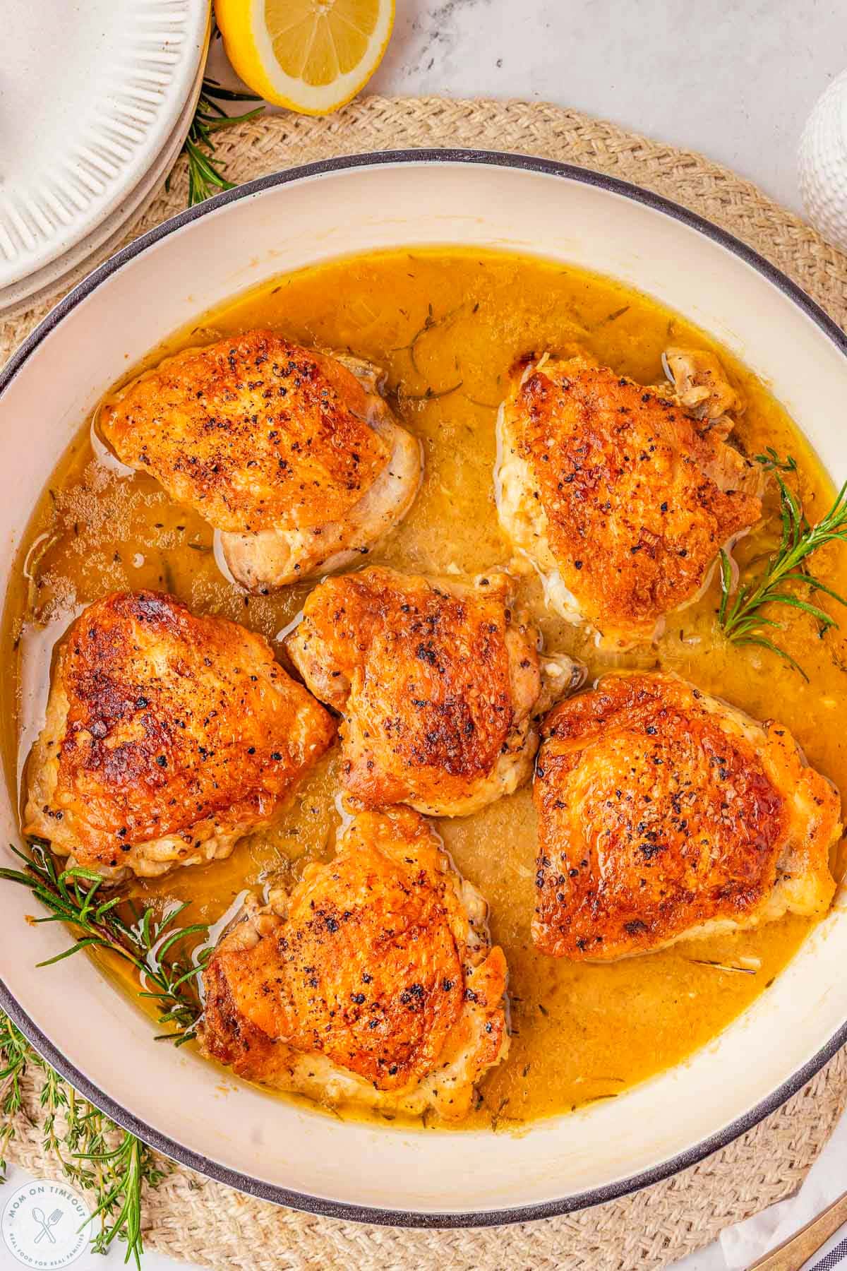 Close up overhead shot of braised chicken thighs in skillet with fresh herbs and lemon.