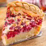 Slice of cranberry custard pie sitting on wood cutting board.